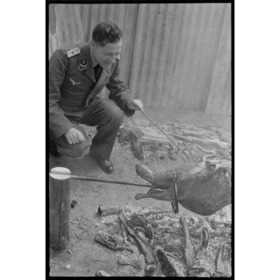 Un lieutenant d'un service administratif de la Luftwaffe surveille la cuisson de la viande lors d'un méchoui organisé au sein d'une unité de reconnaissance de l'armée de l'Air allemande (Aufklärungsgruppe).
