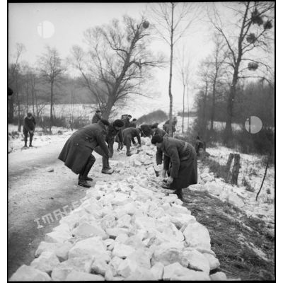 Des pionniers d'une unité de la 55e DI (division d'infanterie) entassent des pierres pour la réfection d'une route.