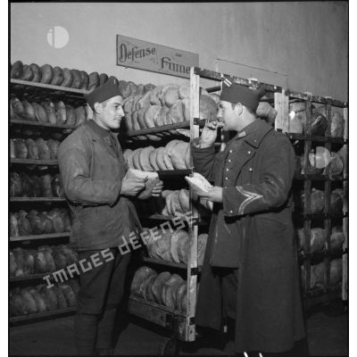 Un sergent de carrière (double galonnage en fer de lance sur la manche) contrôle la qualité du pain produit par une boulangerie militaire.