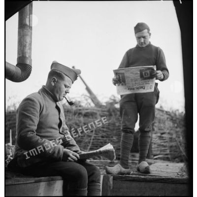 Deux artilleurs du 402e RAAA ou RADCA (régiment d'artillerie antiaérienne ou de défense contre-avions), rattaché à la 32e BDCA (brigade de défense contre-avions), lisent le journal Paris-Soir près d'un poste de combat d'une batterie.