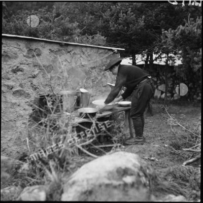 Un soldat de la 5e armée lave de la vaisselle dans des bassines à l'extérieur.