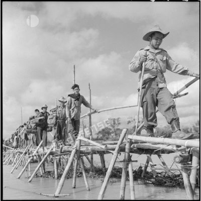 Des éléments du bataillon de marche indochinois (BMI) progressent sur un pont de bambous au cours de l'opération Marécages.
