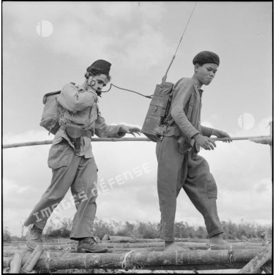 Le transmetteur radio du bataillon de marche indochinois (BMI) et son porteur vietnamien sur un pont de bambous au cours de l'opération Marécages.