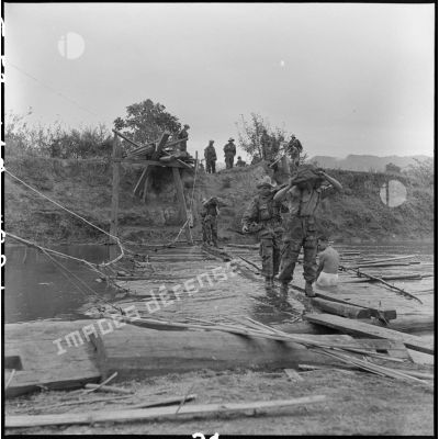 Des éléments du 35e régiment d'artillerie légère parachutiste (RALP) et des partisans franchissent la rivière Nam Youn chargés d’un canon de 75 mm sans recul largué par parachute.
