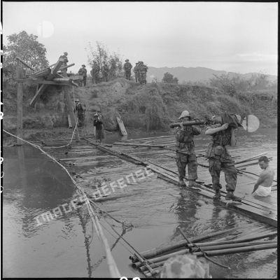 Des soldats du 35e régiment d'artillerie légère parachutiste (RALP) et des partisans franchissent la rivière Nam Youm près de Diên Biên Phu sur un pont de fortune chargés de matériel d'artillerie.