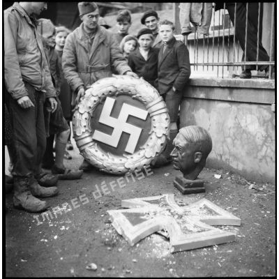 Trophées de guerre dans une rue de Belfort libéré : une couronne avec la croix gammée (le swastika nazi), une sculpture de la croix de fer et un buste d'Hitler.