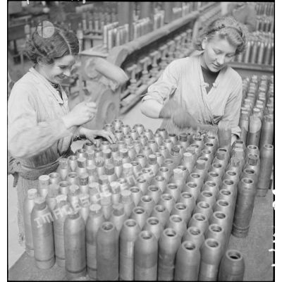 Dans une cartoucherie ou un atelier de fabrication, des ouvrières ferment des enveloppes d'obus de 75 mm avec des bouchons de bois.