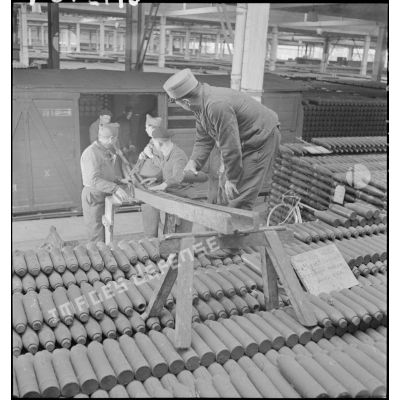 Dans une cartoucherie ou un atelier de fabrication, des ouvriers et des soldats chargent des obus de 75 mm, modèle 1917, dans un wagon de chemin de fer.