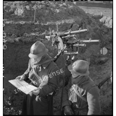 Sur le terrain, deux fantassins, servants de deux mitrailleuses jumelées Hotchkiss modèle 1914 de 8 mm, sur affût antiaérien, lisent un numéro du journal de campagne intitulé Le tireur debout.