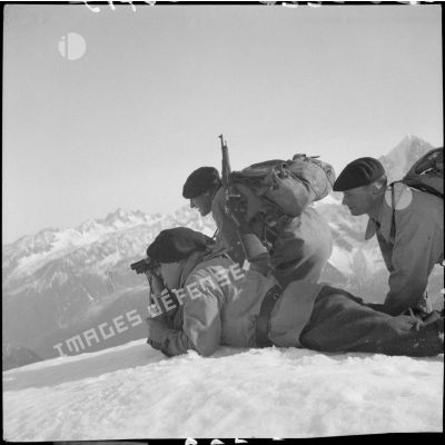 Trois éclaireurs du 199e BCHM allongés ou à genoux dans la neige observent aux jumelles.