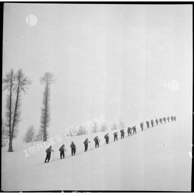 Une section d'éclaireurs-skieurs en mission de reconnaissance gravit une pente enneigée.
