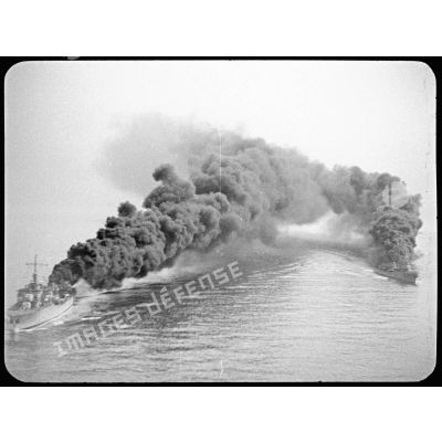 Vue aérienne sur deux navires de la Marine nationale, probablement un torpilleur et un contre-torpilleur, dont les cheminées émettent une fumée épaisse.