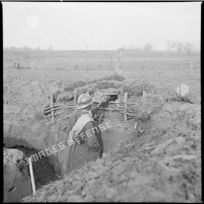 Dans une tranchée un soldat est photographié en plongée de dos dans son poste de tir.