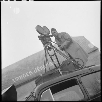 Un caméraman filme installé sur le toit d'une voiture.