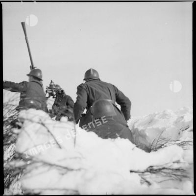 Dans la neige, une équipe de pièce du 404e RAAA se précipite vers le canon de 25 mm CA visible en arrière-plan.