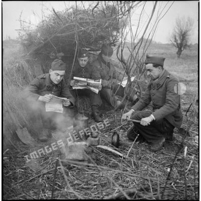 Photographie de groupe de quatre soldats du 6e Cuirassiers qui lisent près d'un feu où chauffe une gamelle.