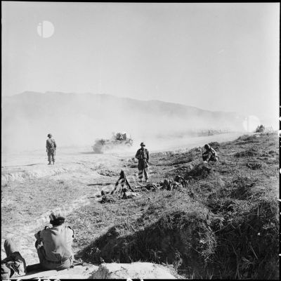Circulation sur la route qui traverse le camp de Diên Biên Phu tandis que des soldats sont au repos sur le bas-côté.