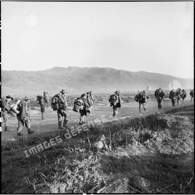 Des soldats portant leur paquetage avancent sur le piste vers un centre de résistance du camp de Diên Biên Phu.