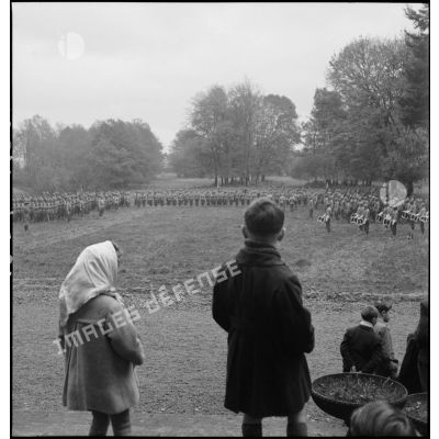 Prise d'armes au 2e RD dans le parc d'une demeure. Au premier plan, quelques habitants observent la cérémonie.