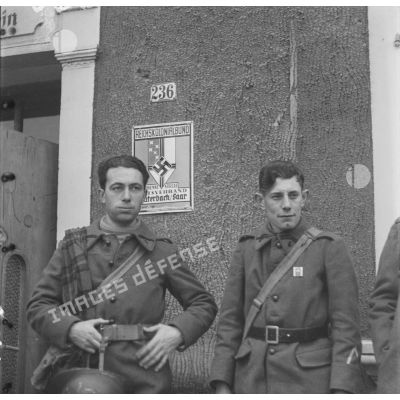 [Une équipe du SCA, photographes et cameramen, se trouve devant l'entrée de la Ligue coloniale du Reich à Lauterbach. A droite, le maréchal des logis  André Bauduin et à gauche le soldat Henri Goupy. Septembre-ocobre 1939.]