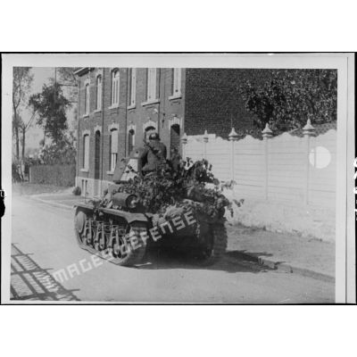 Un char léger Hotchkiss M35/39 H de la 3e DLM est photographié en plan général de trois quarts arrière alors qu'il se déplace dans une rue d'un village belge.