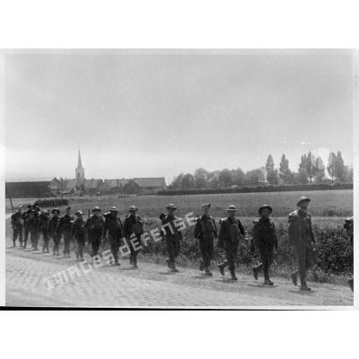 Plan général de soldats de la BEF qui marchent en colonne sur une route pavée à la sortie d'un village.