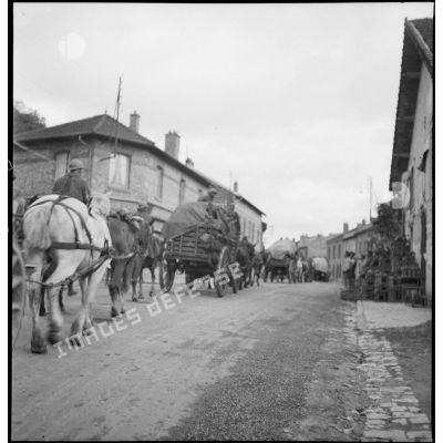 Un convoi hippomobile de la 2e armée traverse un village, il est photographié en plan général de trois quarts.