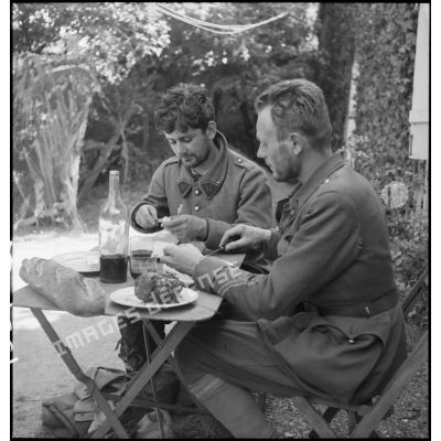 Deux sous-officiers du 11e RC évadés des lignes allemandes mangent attablés à une table de campagne.