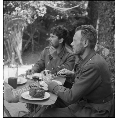 Deux sous-officiers du 11e RC évadés des lignes allemandes mangent attablés à une table de campagne.