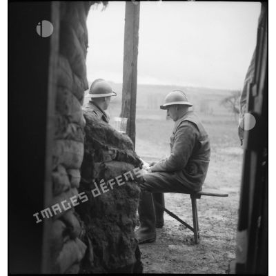 A l'entrée d'un abri fortifié de la 2e armée, deux soldats assis lisent un journal.