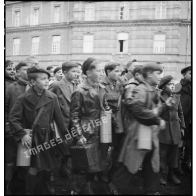 Photographie de groupe d'élèves qui rentrent en classe, les enfants portent en bandoulière des containers métalliques d'ANP.