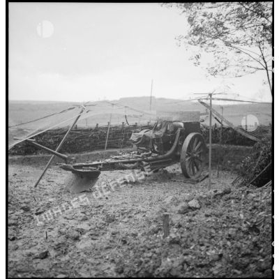 Sous un filet de camouflage une pièce de 155 mm court M1915/17 est photographiée de trois quarts dos.