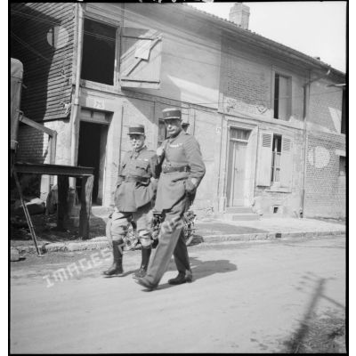Deux officiers marchent dans une rue de village.