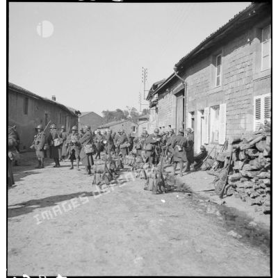 Dans une rue de village une section d'infanterie fait une halte.