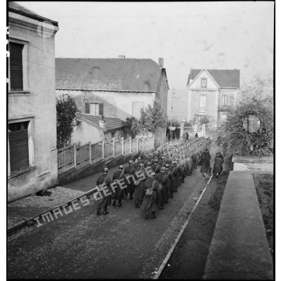 Des soldats de la 2e armée défilent en unité constituée dans une rue de village.