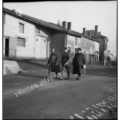 Trois cadres de la 2e armée marchent dans une rue de village.