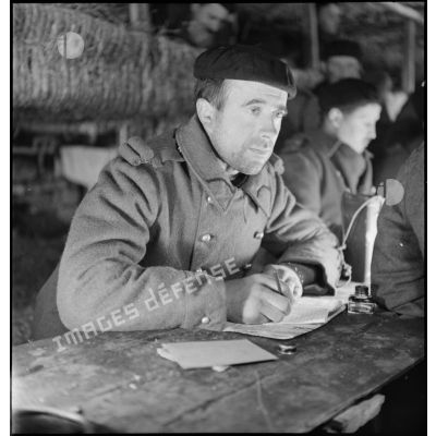 Portrait d'un soldat de la 2e armée qui écrit une lettre à l'intérieur d'un abri de campagne.