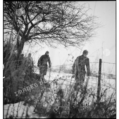 Près de la frontière belge une colonne de soldats en patrouille se déplace le long d'un champ enneigé.