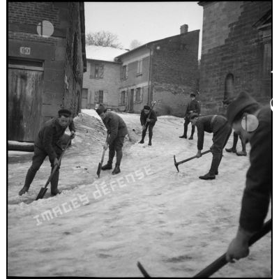 Plan général de soldats qui déblayent de la neige accumulée dans la rue d'un village.