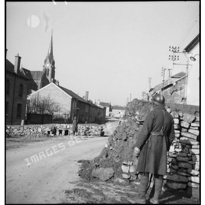 Plan général en enfilade d'une rue de village où des soldats de la 2e armée montent la garde derrière des chicanes de pierre.