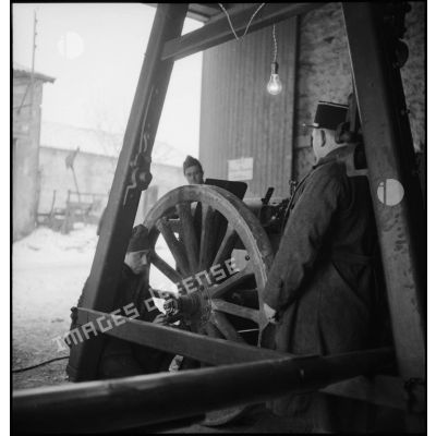 Sous un toit de hangar des soldats démontent la roue d'un affût de canon.
