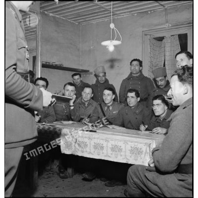 Assis autour d'une table des sous-officiers du 15e RTA écoutent un lieutenant.