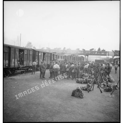 Dans une gare, près de wagons, une troupe de la 2e armée est en attente.