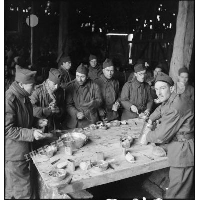 Photographie de groupe de soldats de la  2e armée qui mangent debout autour d'une table dans une grange.