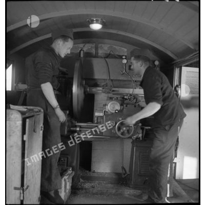 Deux mécaniciens travaillent sur une machine-outil dans une remorque de l'atelier de réparation de campagne.