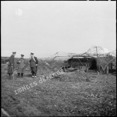 Des officiers britanniques discutent avec un officier français près d'une pièce d'artillerie camouflée.