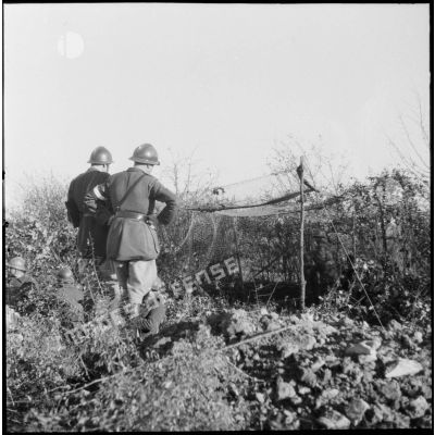 Deux officiers de la 3e armée photographiés de dos regardent un camouflage de pièce d'artillerie.