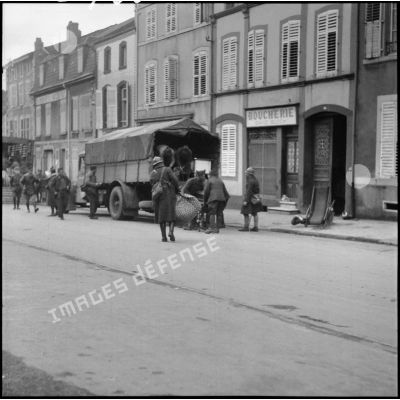 Plan général de soldats de la 3e armée qui chargent des camions dans une rue de village de la Moselle.