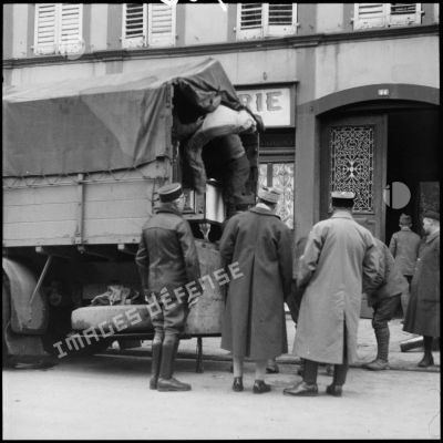 Des soldats de la 3e armée chargent un camion dans une rue de village de la Moselle. Un général les regarde.