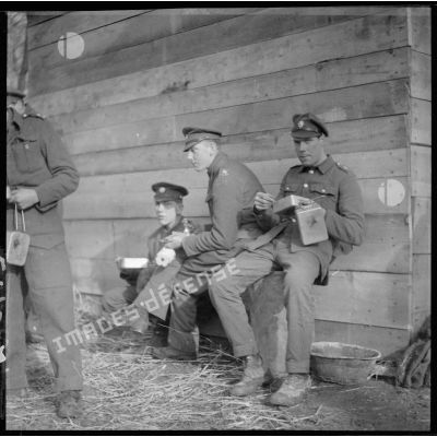 Des soldats anglais de la BEF mangent assis près d'un baraquement.